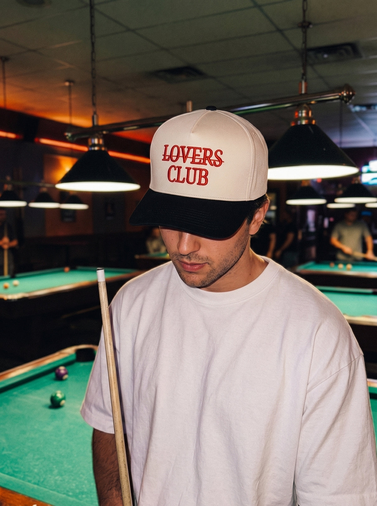 Person wearing a 'Lovers Club' cap in a pool hall setting